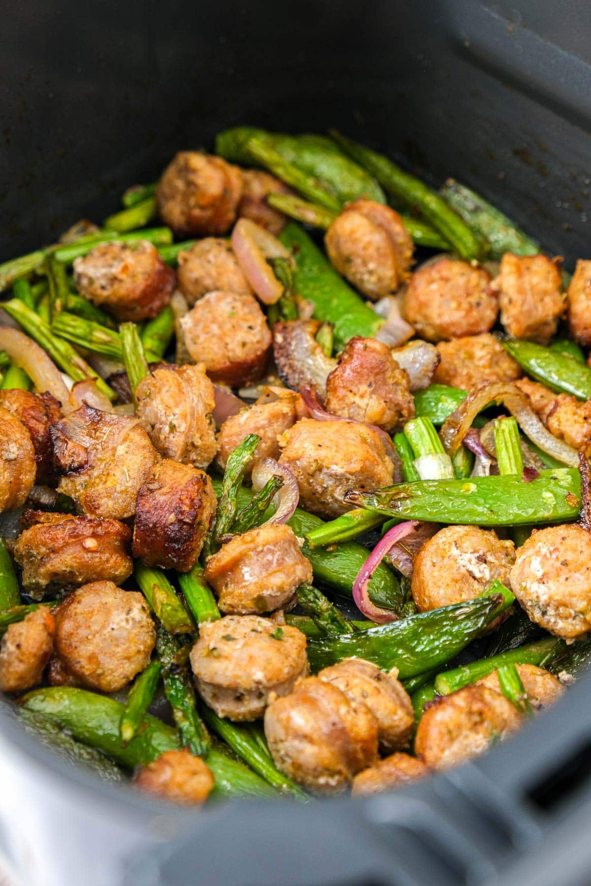 cooked vegetables and sausage in air fryer basket.