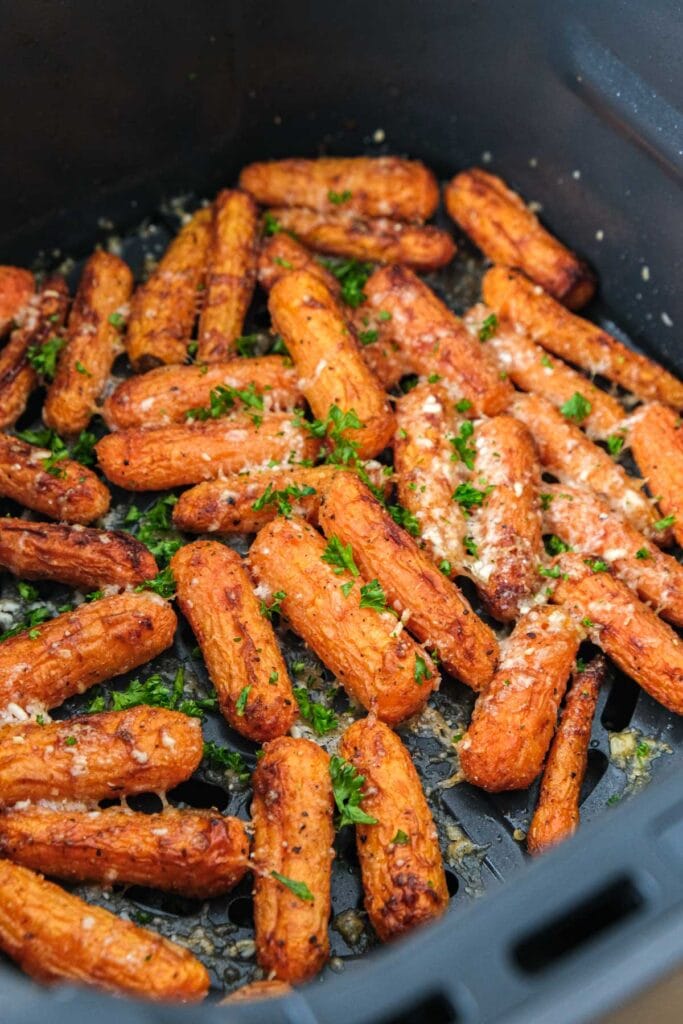 parmesan baby carrots in air fryer basket with parsley on top.
