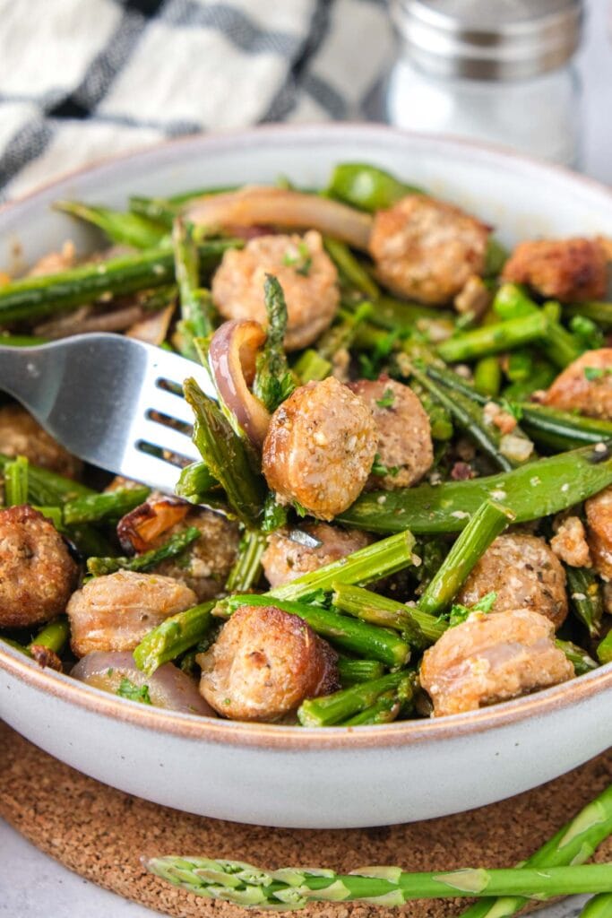 sausage and vegetables in bowl with silver fork piercing some.