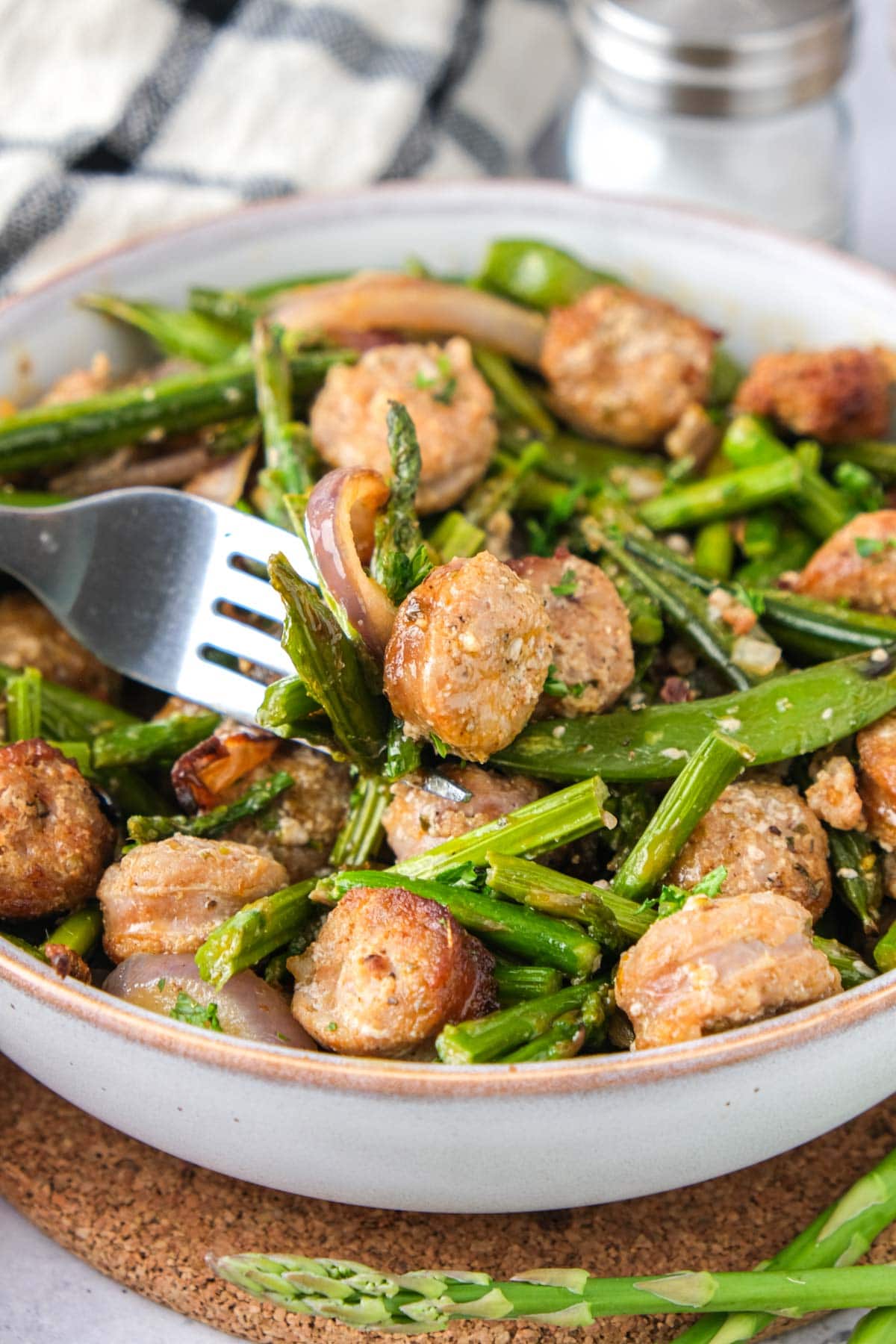 sausage and vegetables in bowl with silver fork piercing some.