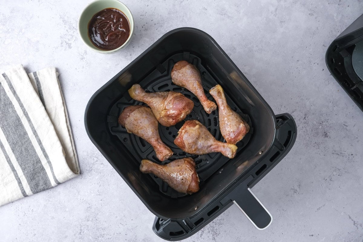 raw chicken drumsticks in air fryer basket sitting on counter.