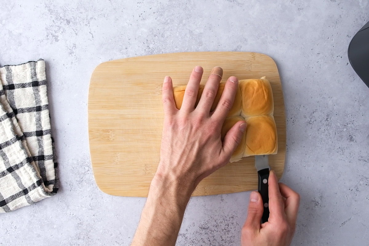 hand cutting block of slider buns in half on counter.