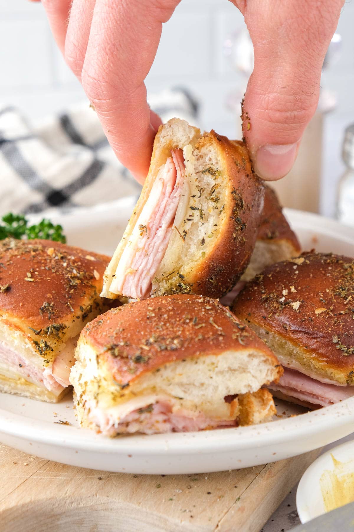 hand picking ham and cheese slider up from pile of sliders on plate.