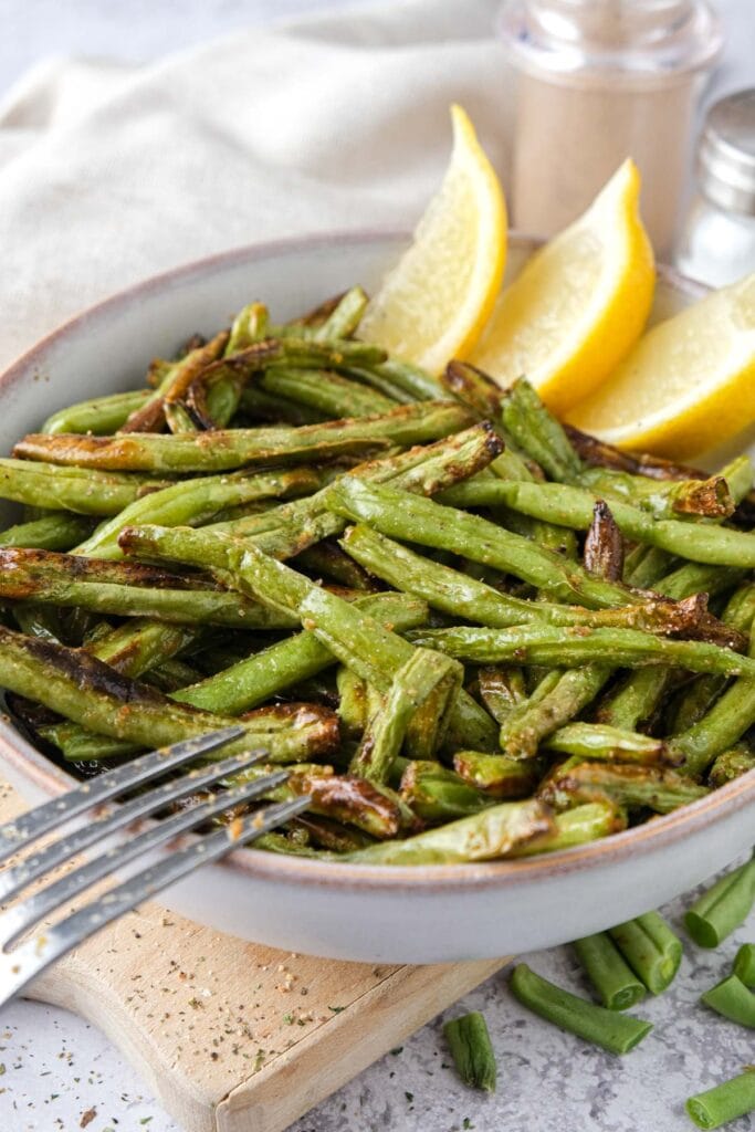 cooked green beans in a bowl with lemon wedges behind.