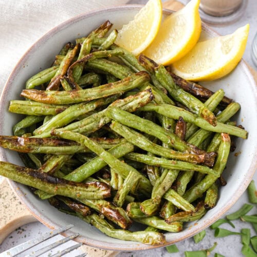 bowl of lemon garlic green beans on wooden board with lemon wedges behind.