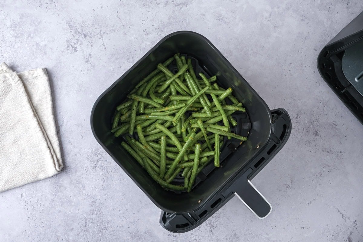 raw green beans covered in spices in black air fryer basket.
