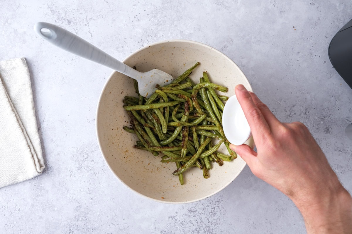 hand pouring lemon juice into bowl of cooked green beans.
