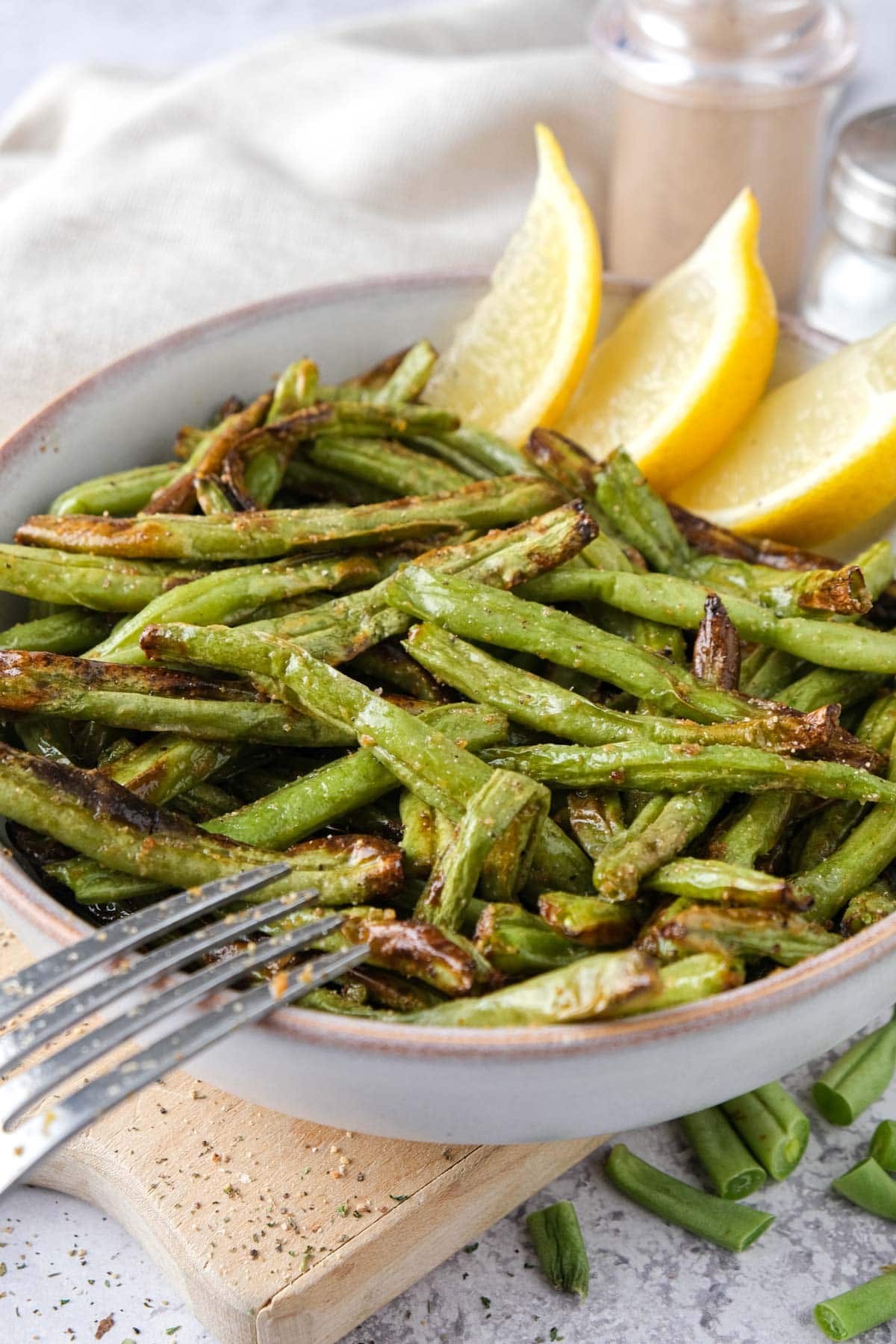 cooked green beans in a bowl with lemon wedges behind.