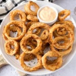 plate covered in crispy onion rings with dip behind.