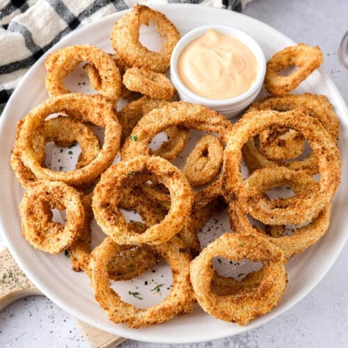 plate covered in crispy onion rings with dip behind.