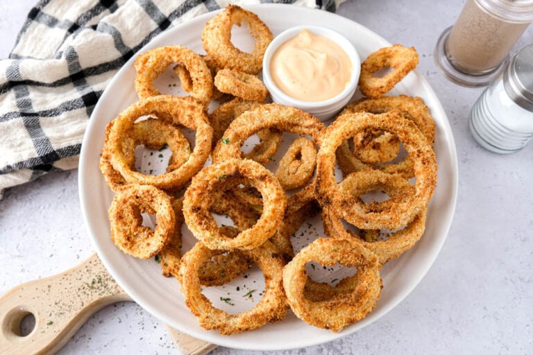 plate covered in crispy onion rings with dip behind.
