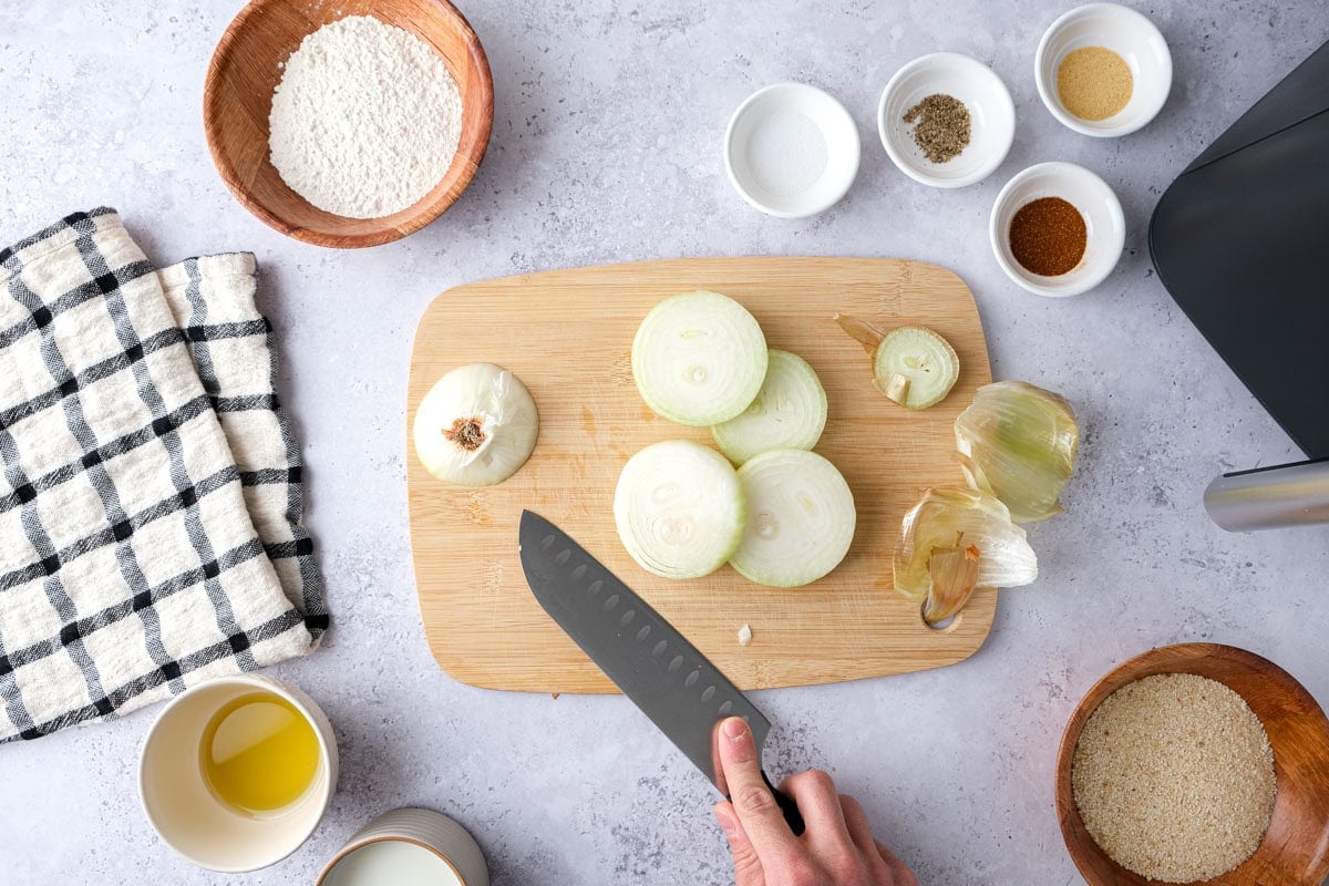 yellow onion being cut on cutting board with ingredients around.