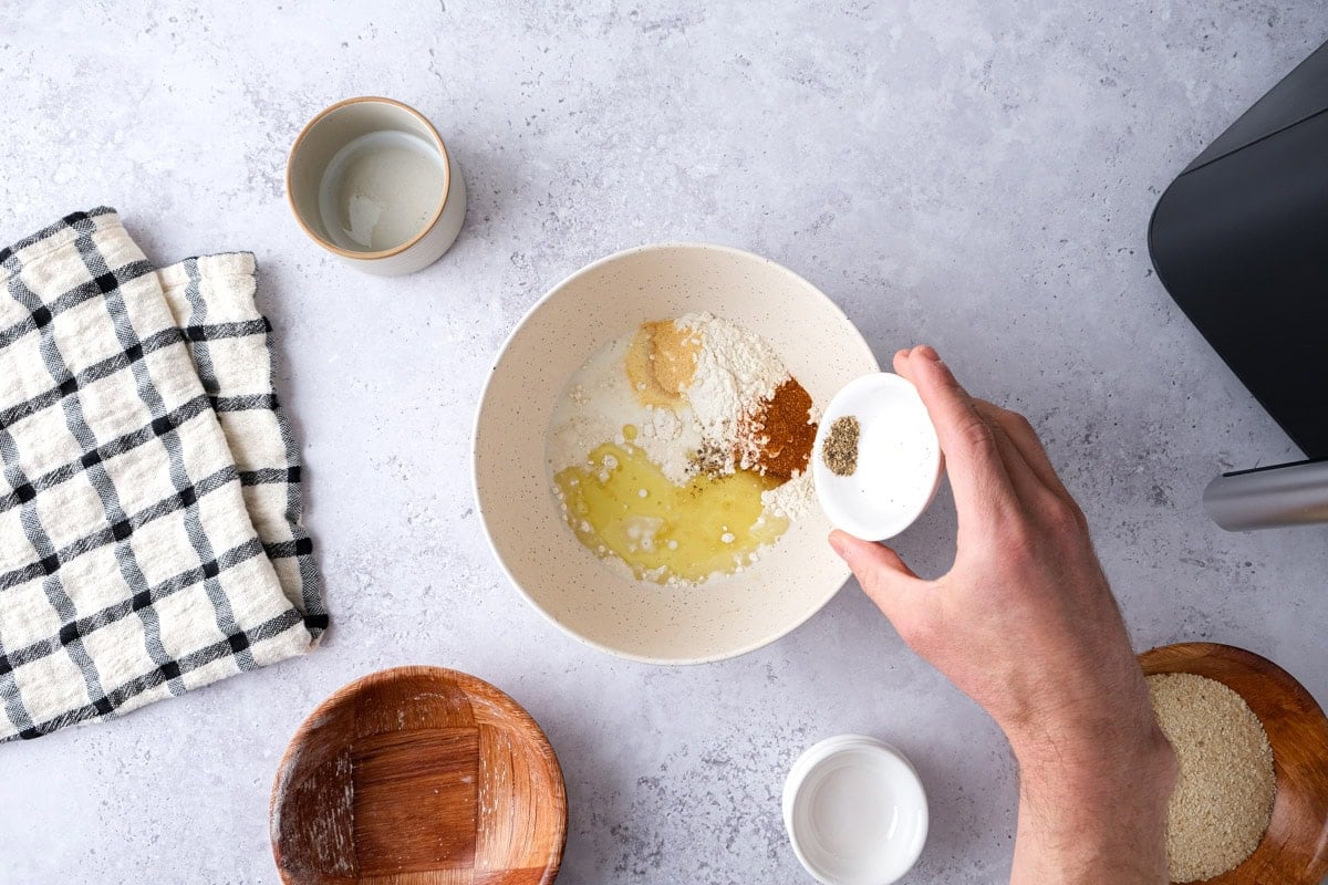 ingredients to make batter being poured into mixing bowl on counter.