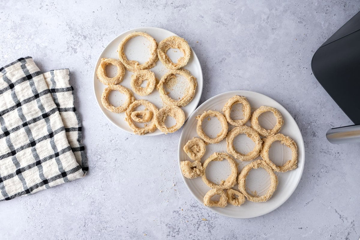 raw breaded and battered onion rings on plates on counter.
