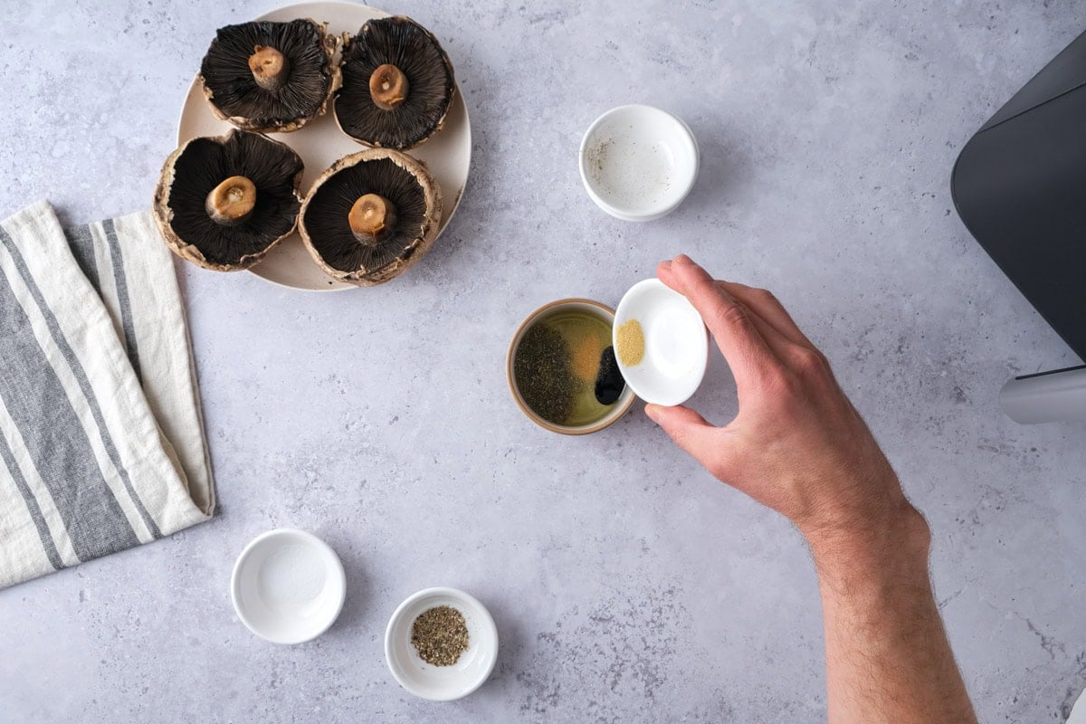 hand pouring spices into oil in smaller bowl on counter.