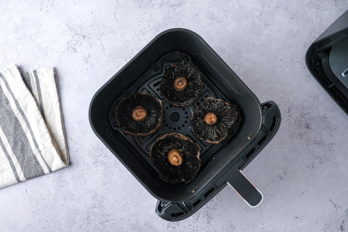 four raw portobello mushrooms in air fryer basket on counter.