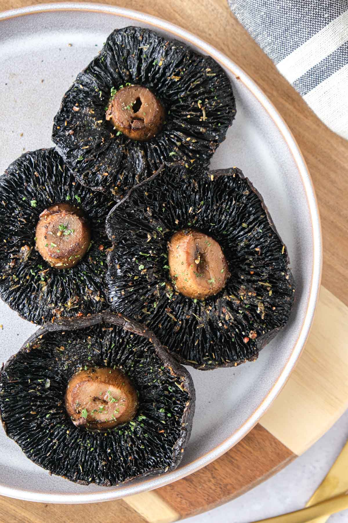 cooked and seasoned portobello mushrooms on plate on wooden board.