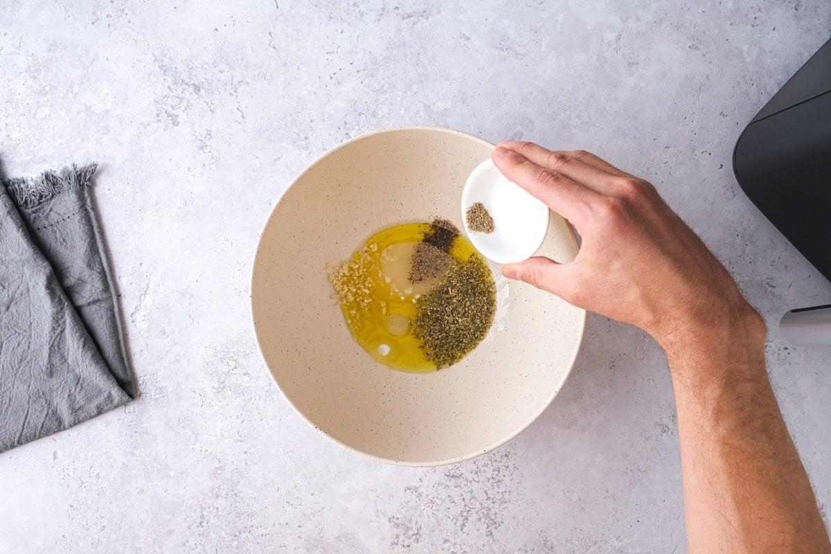 hand adding spices into bowl on counter.