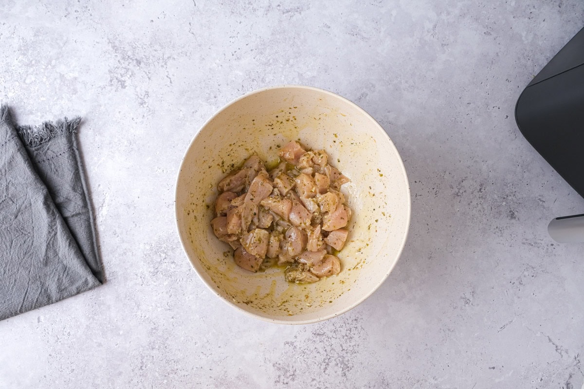 raw chicken pieces coated in greek marinade in bowl on counter.
