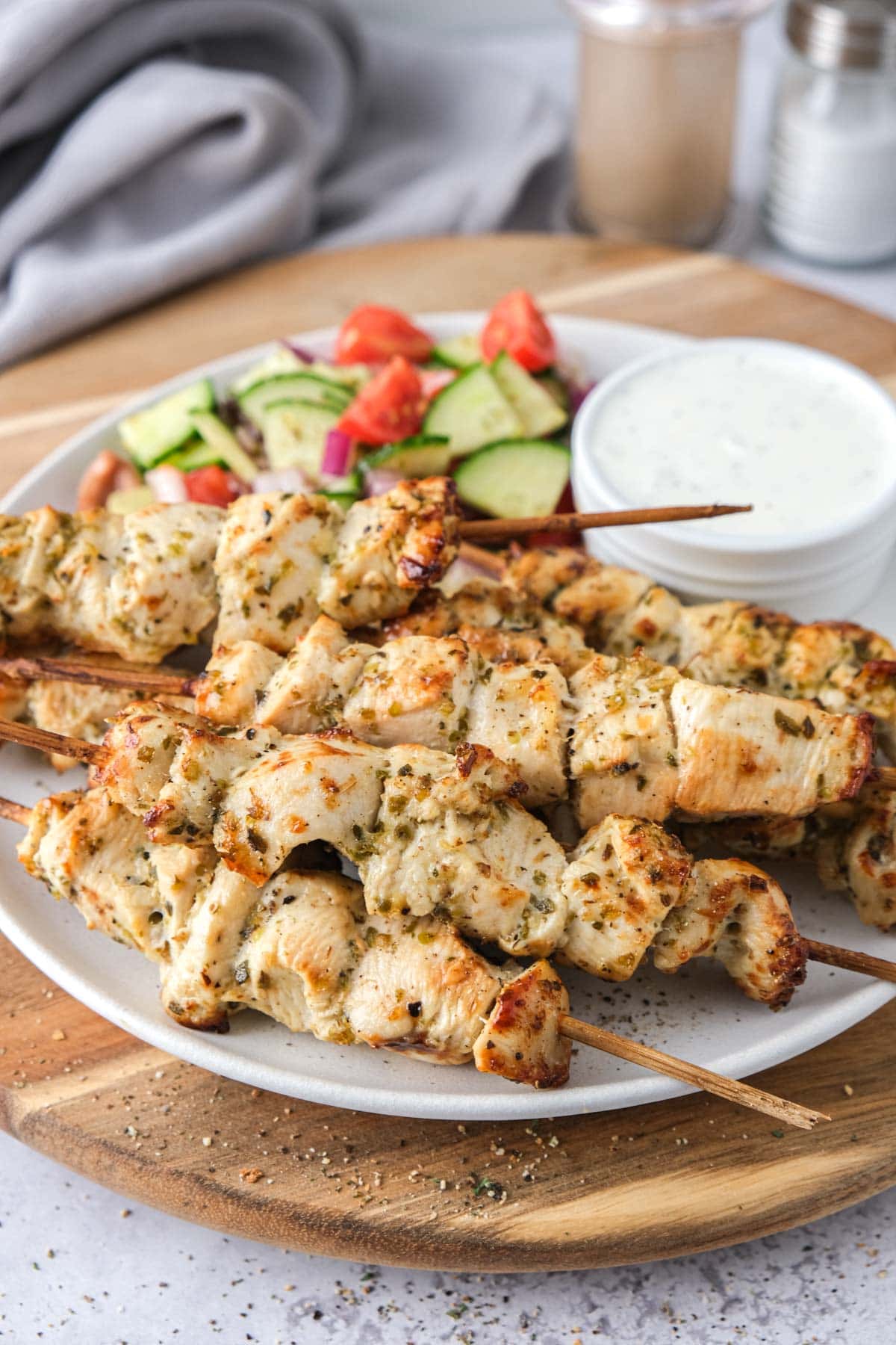 chicken souvlaki skewers on plate with salad and sauce behind.