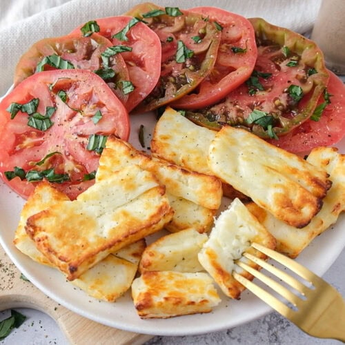 plate of air fryer halloumi cheese on wooden board with fork in front.