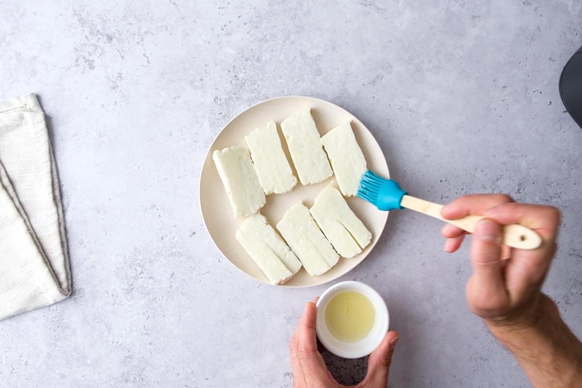 hand brushing oil onto slices of halloumi cheese on plate.