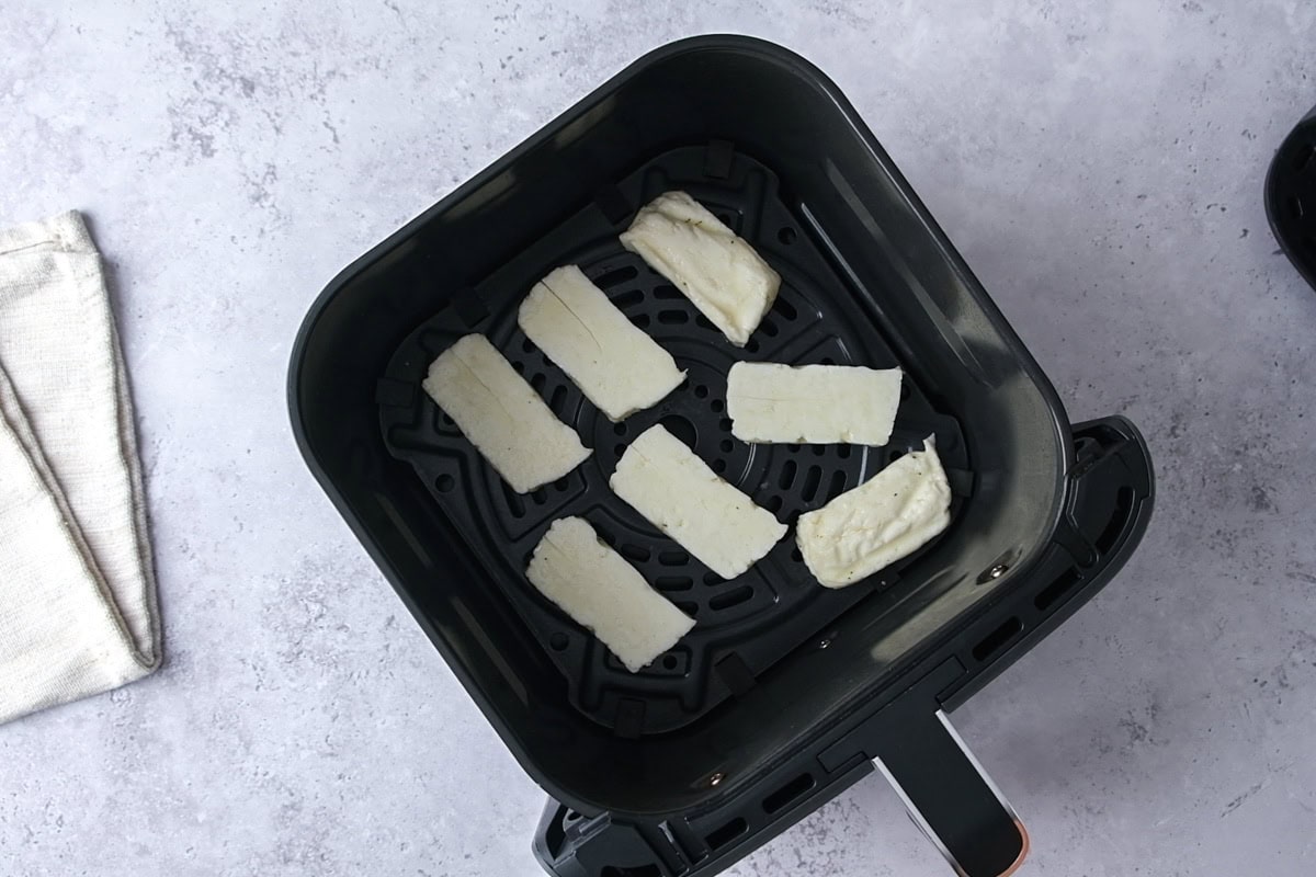 slices of halloumi cheese in air fryer basket on counter.