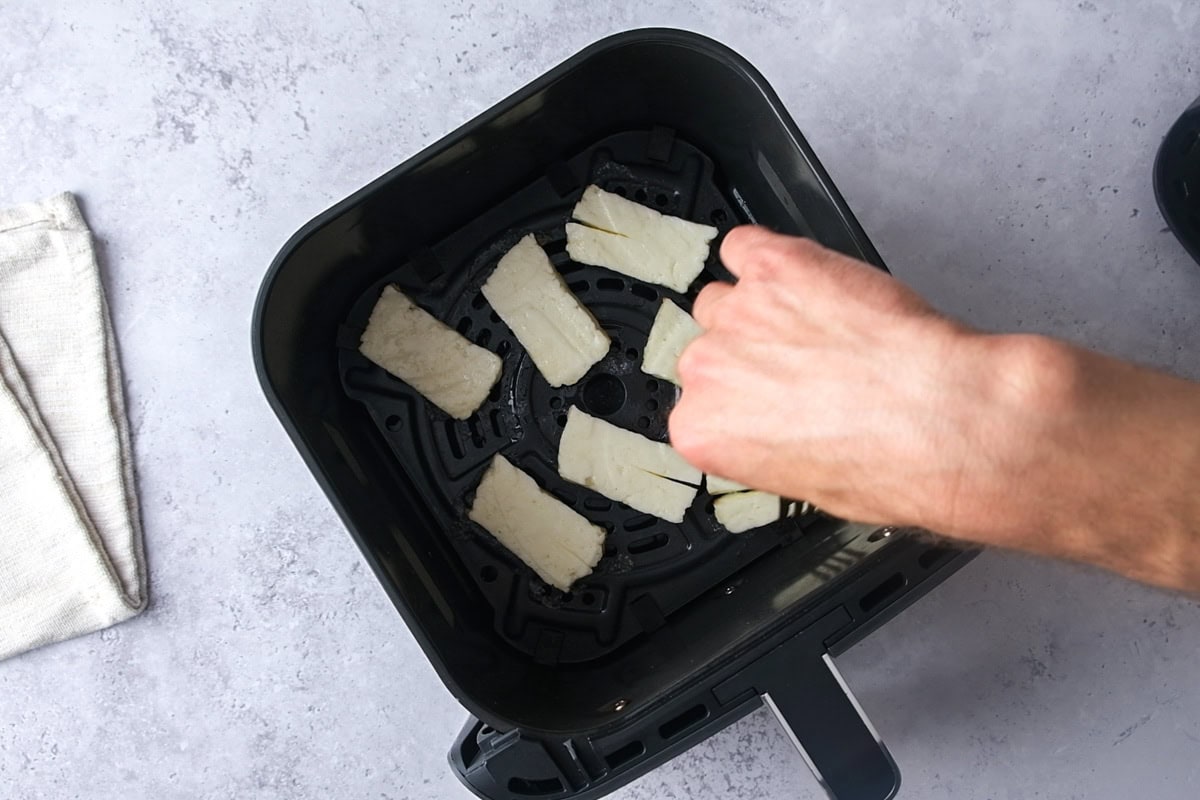hand flipping halloumi cheese in air fryer basket.