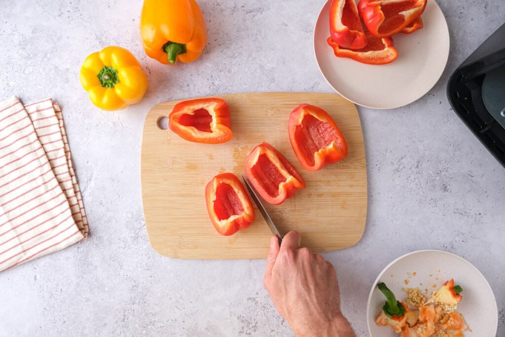 red bell pepper being cut on wooden cutting board with yellow bell pepper next to it.