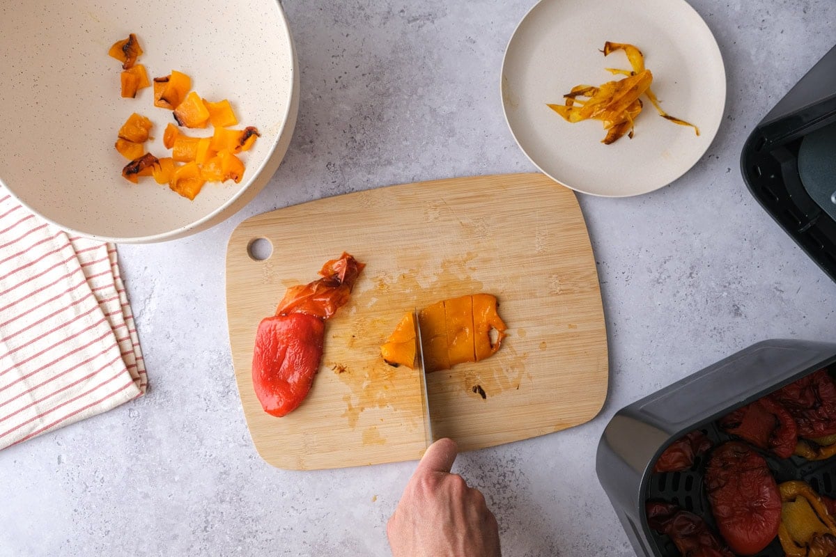 roasted bell pepper slices with skin removed being cut on wooden board. 