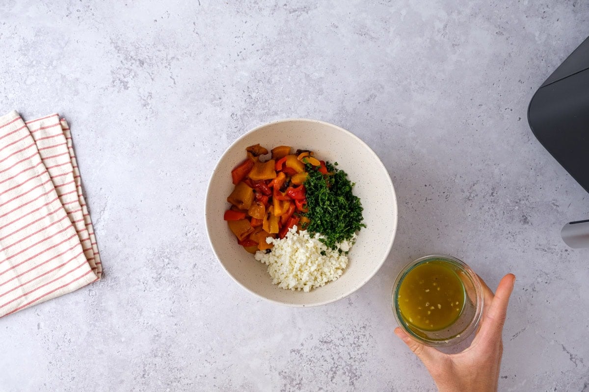 roasted bell pepper pieces, chopped parsley, and feta in bowl with dressing in jar next to it.