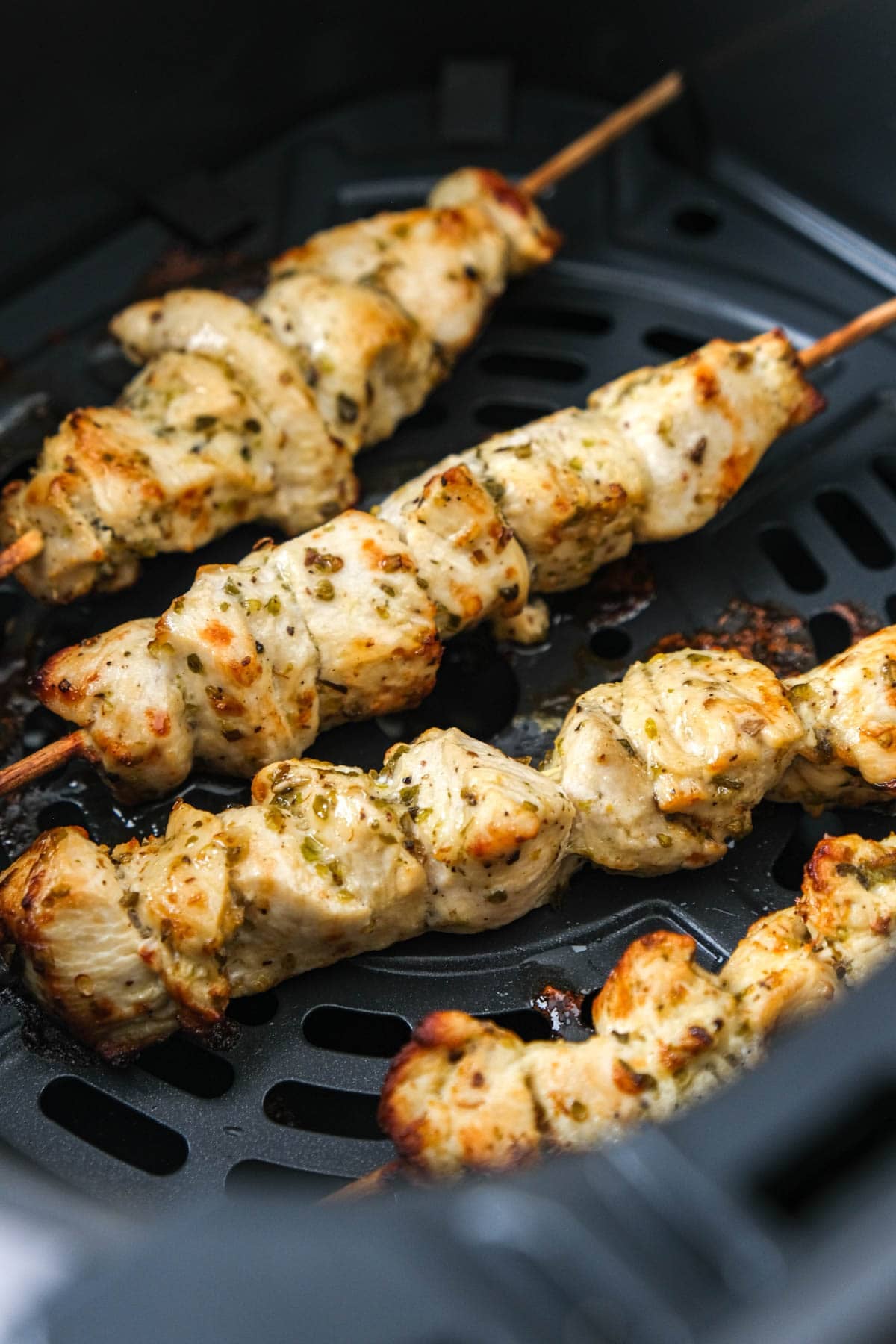four cooked chicken souvlaki in air fryer basket.