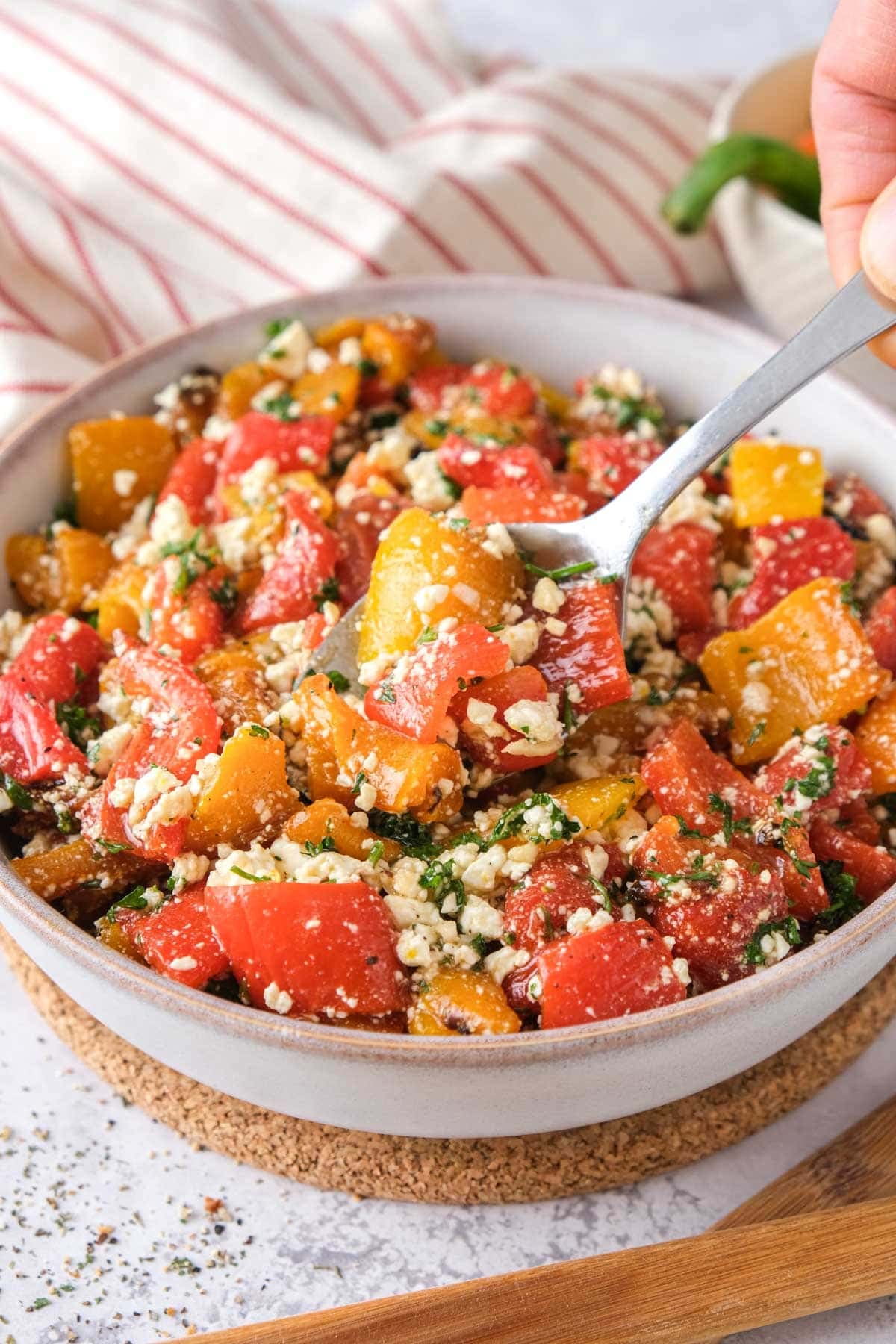 bowl of roasted pepper salad on cork with silver spoon scooping some out.