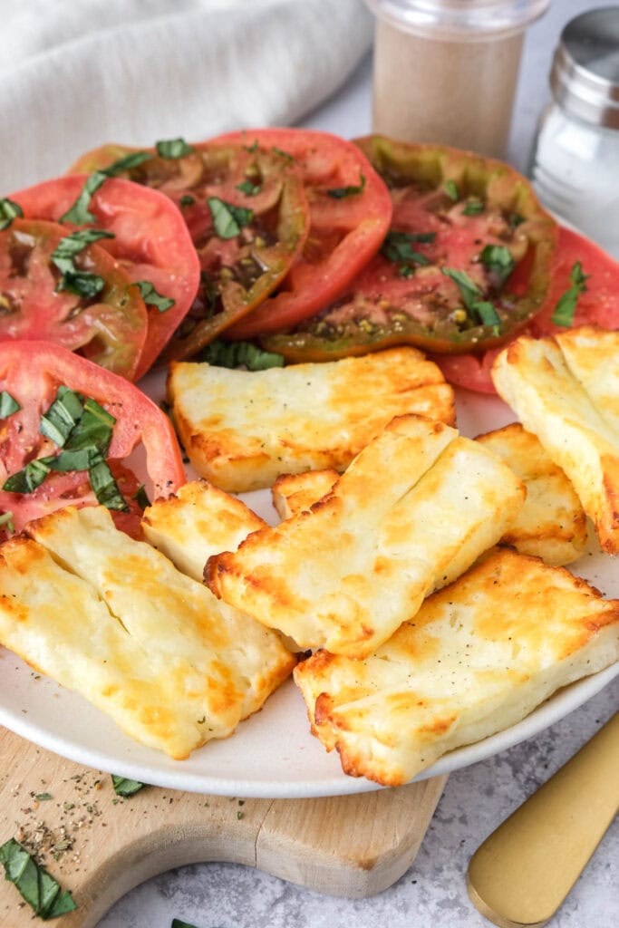 plate of grilled halloumi cheese with sliced tomatoes.