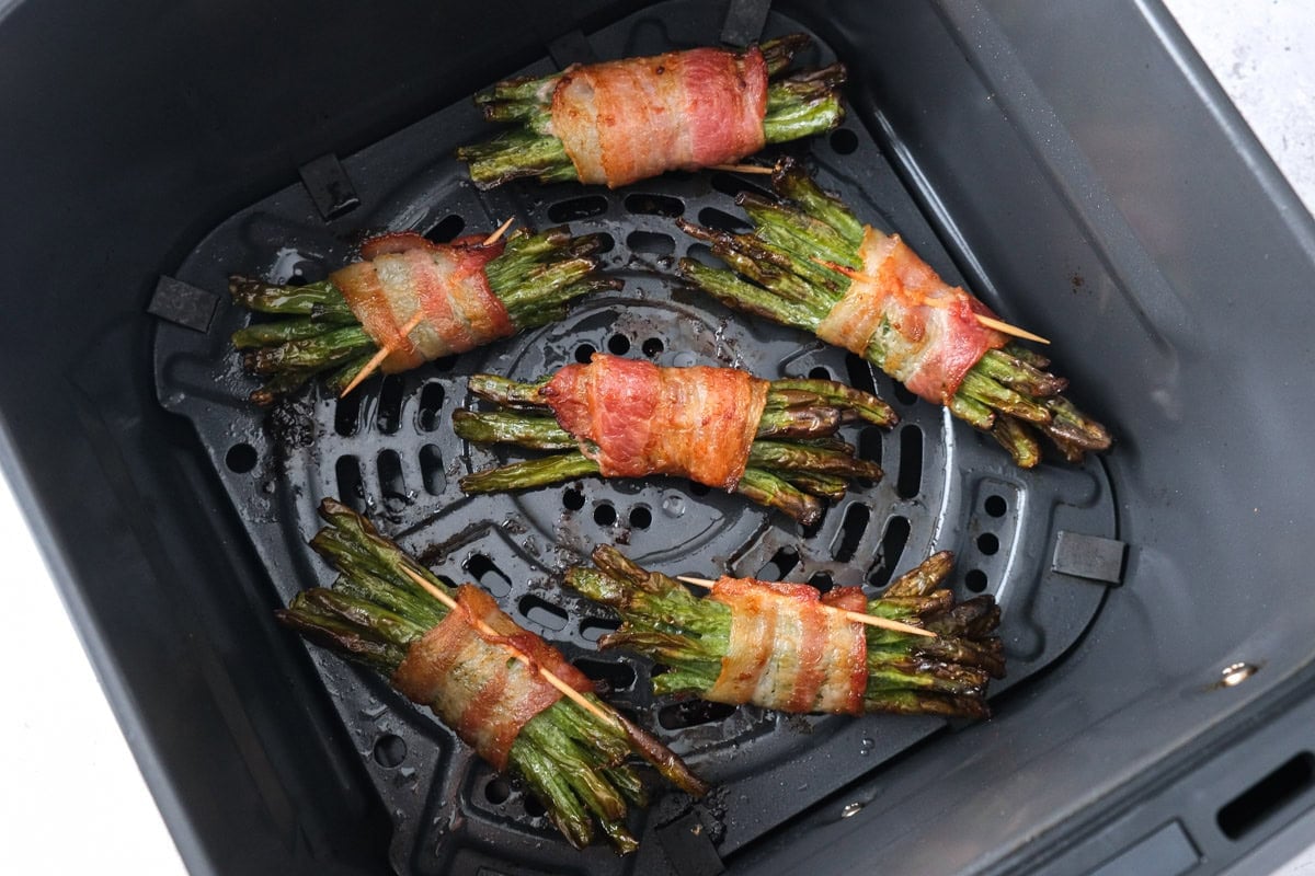 cooked bacon wrapped bundles of green beans in air fryer basket.