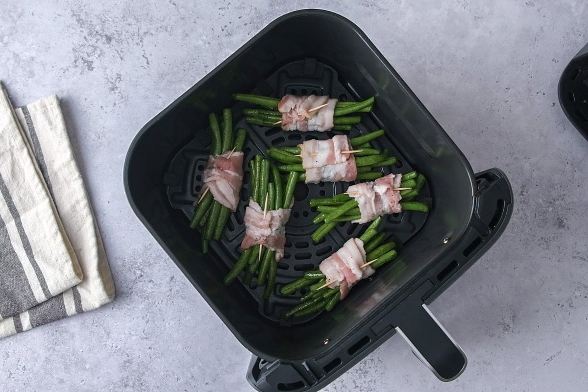 six bundles of green beans wrapped in bacon sitting in air fryer basket.