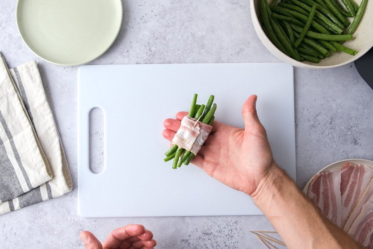 hand holding bundle of green beans wrapped on bacon with counter under.