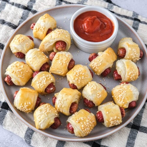 plate of homemade pigs in a blanket with ketchup on plate on dish.