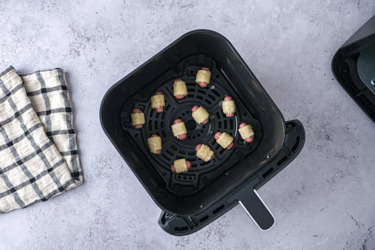 raw pigs in blankets sitting in black air fryer basket on counter.