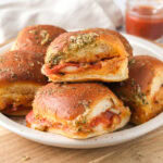 plate of pizza sliders on wooden cutting board.