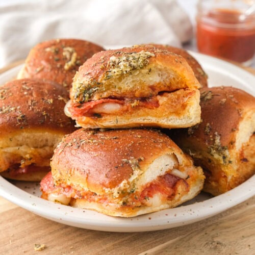 plate of pizza sliders on wooden cutting board.
