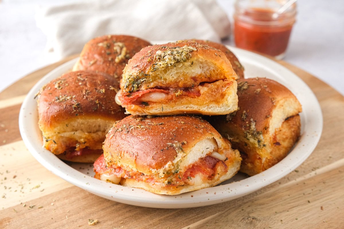 plate of pizza sliders on wooden cutting board.