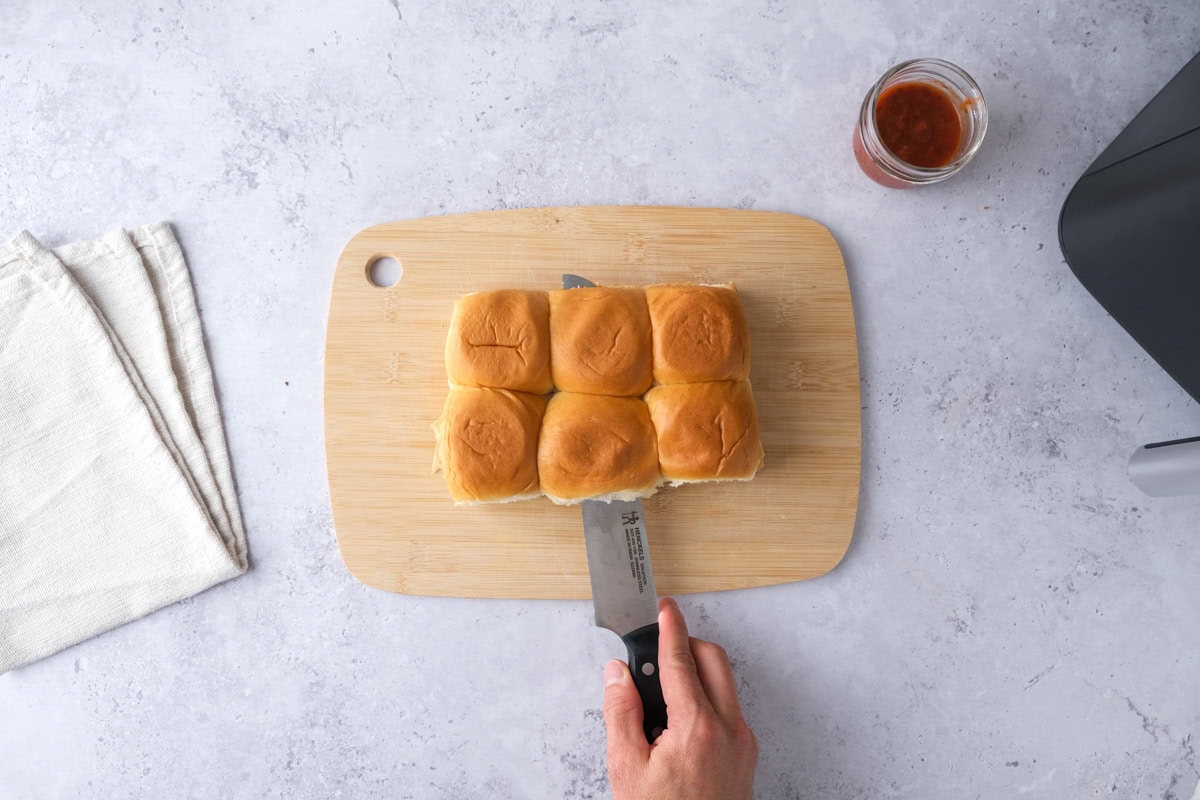 knife cutting through slider buns on cutting board.
