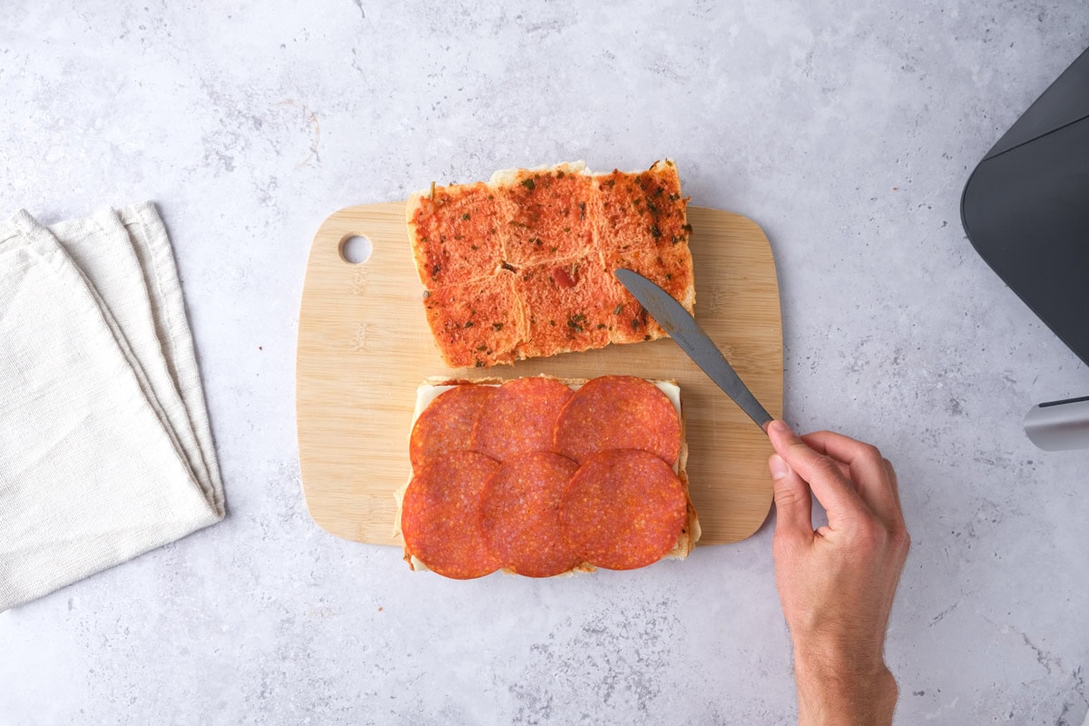 knife spreading pizza sauce on top of slider buns with bottom beside.