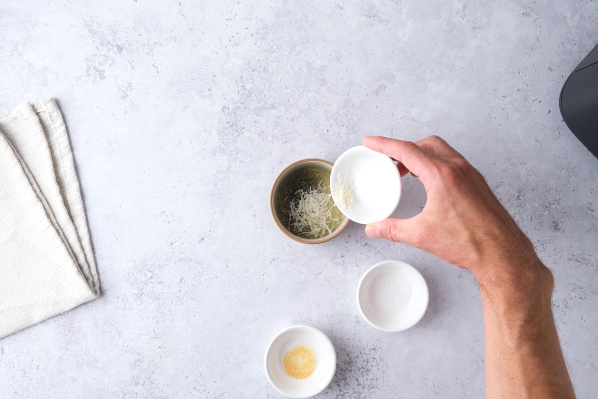 hand with salt in dish pouring more seasonings into small ramekin.