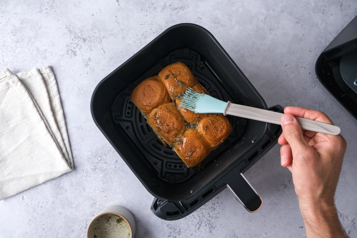 hand with silicone brush spreading oil-spice blend onto slider buns.