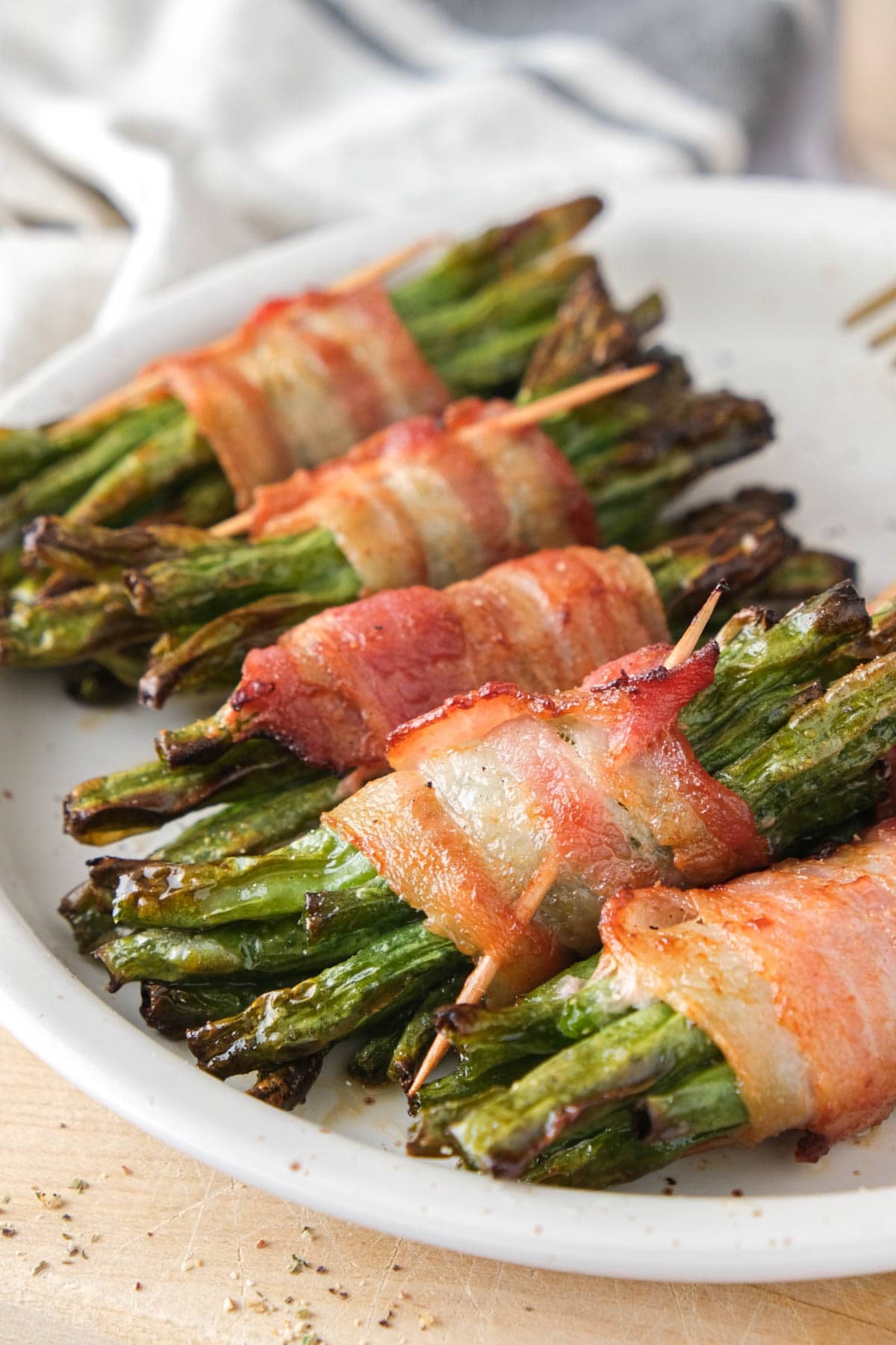 bacon wrapped green beans on plate with wood underneath.