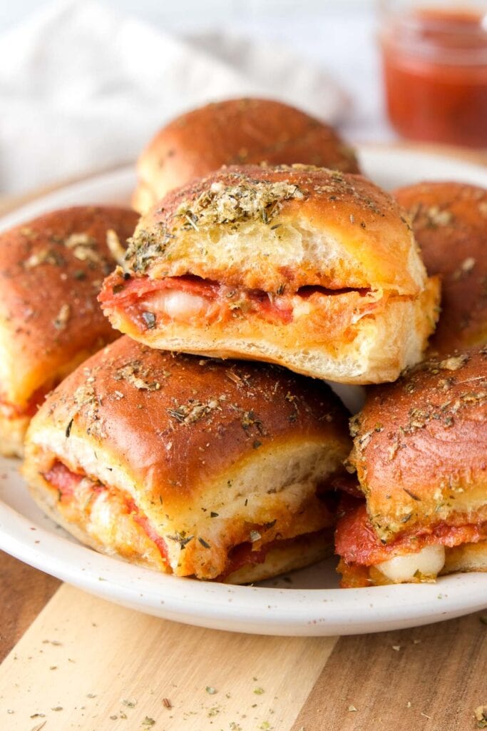 pizza sliders stacked on a plate with sauce behind.