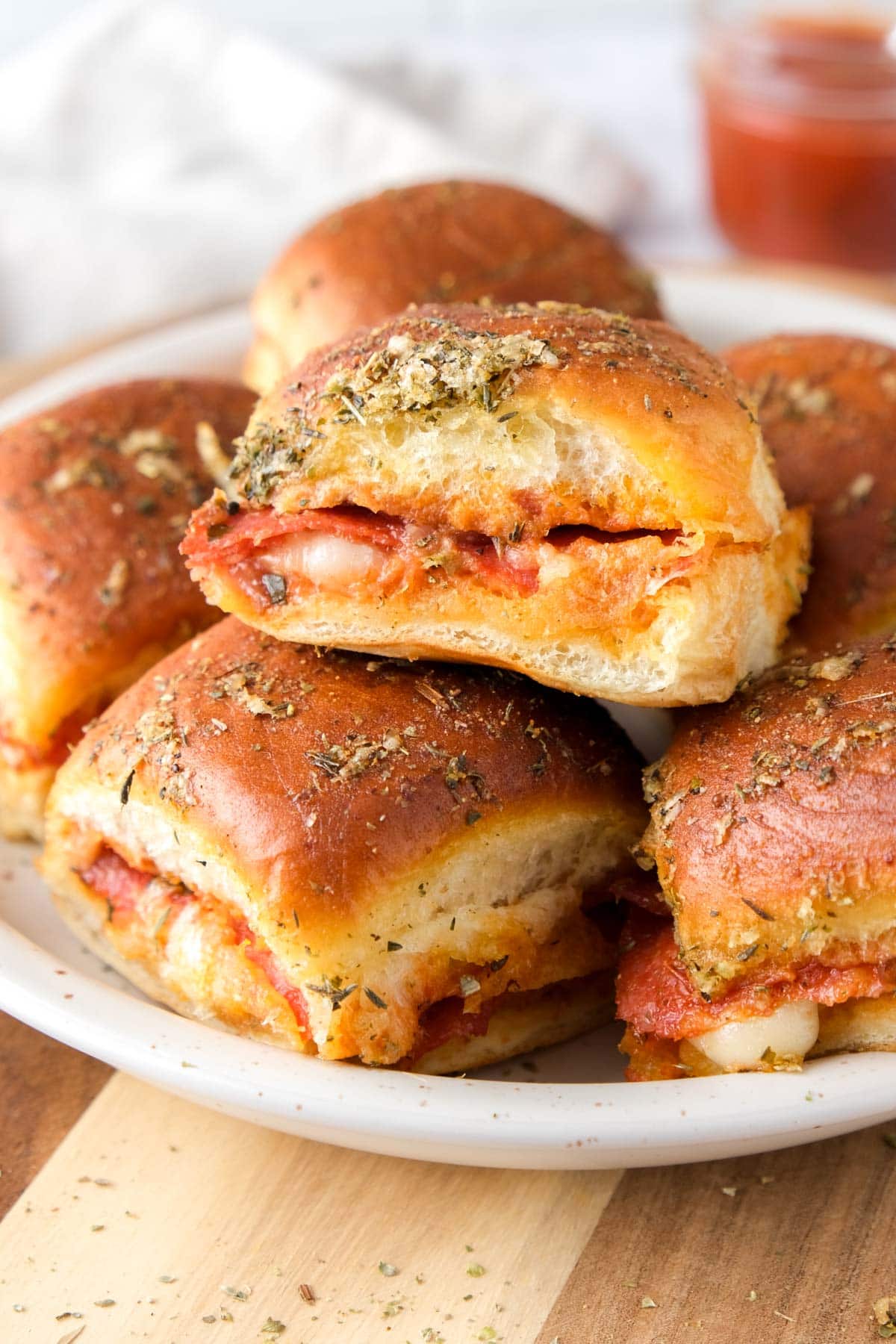 pizza sliders stacked on a plate with sauce behind.