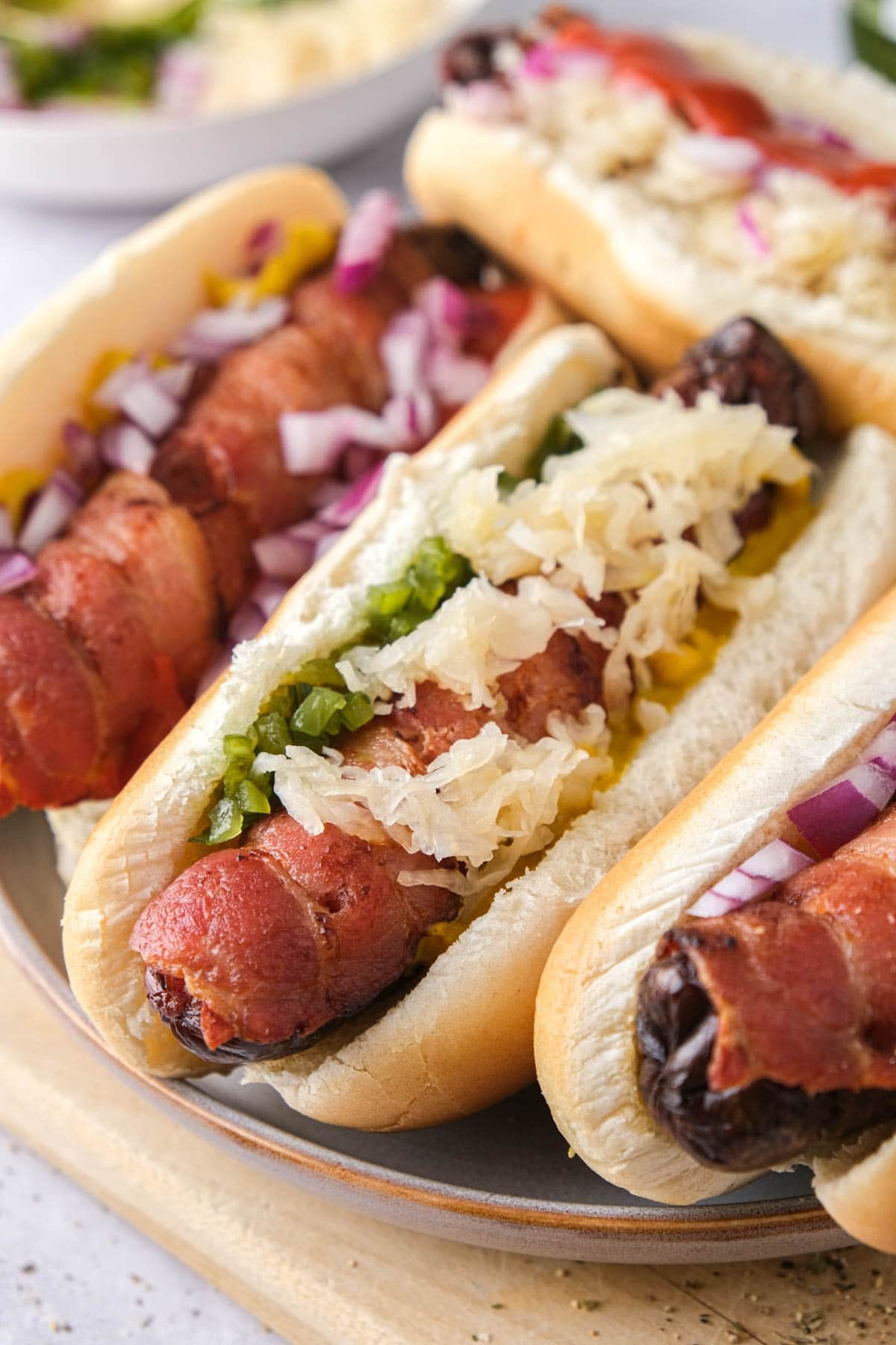 bacon wrapped hot dogs with toppings on plate.
